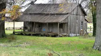An abandoned single-story home in rural Tunica County, Mississippi, with a sagging roofline and weathered wood siding against an overcast sky. Contemporary photograph of housing stock in the county that ranks 16th of 3,144 nationally for household financial distress in July 2026.