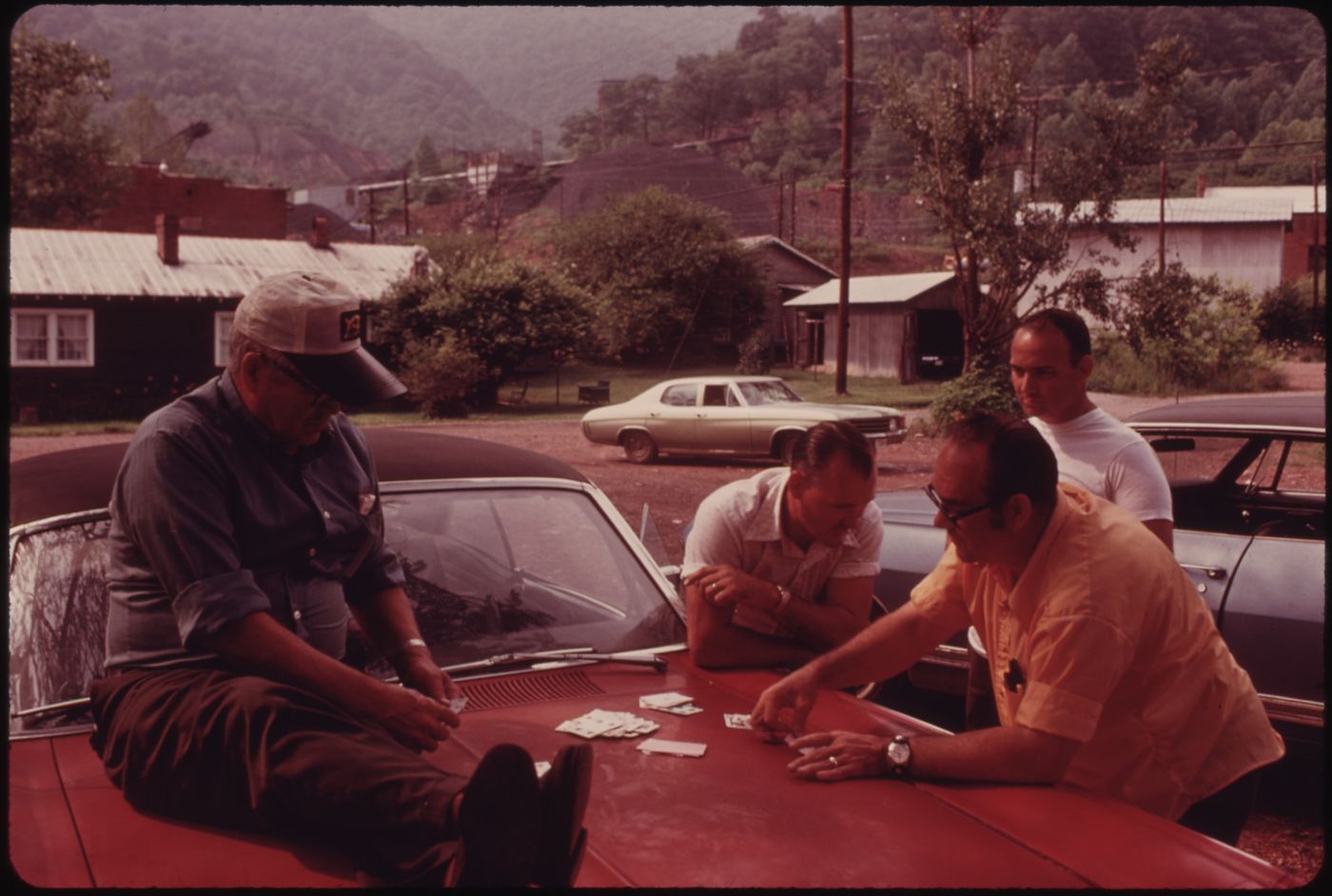Miners playing cards on the hood of a car during the Brookside Mine strike in Harlan County, Kentucky, 1974. The mine is visible in the background.