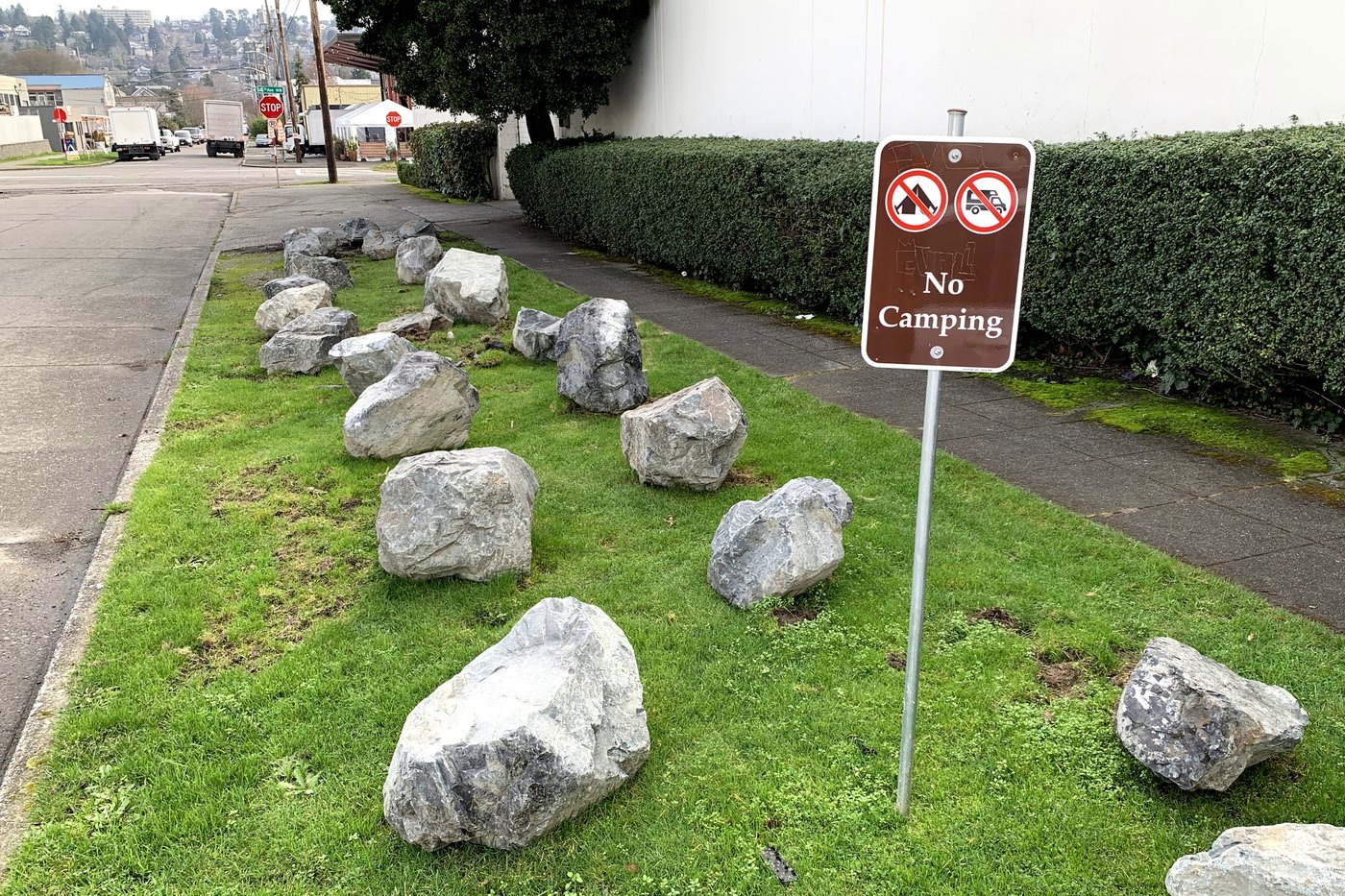A 'No Camping' sign and large boulders placed in a grassy parking strip in Ballard, Seattle. Hostile architecture designed to prevent sleeping in public space.